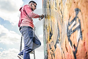 Tattooed graffiti writer painting with color spray on the wall - Contemporary artist at work - Urban lifestyle,street art concept