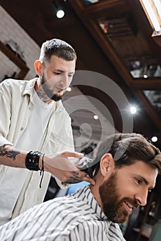 Tattooed hairdresser trimming hair of smiling