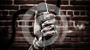 A tattooed male hand holding a microphone against a brick wall. generative ai.