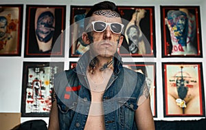 Tattooed man in denim vest and sunglasses in studio