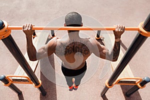 Tattooed man doing pull up exercise, top view