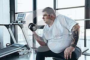 Tattooed man exercising with dumbbell at sports center