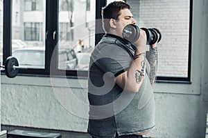 Tattooed man exercising with dumbbells at gym with copy space