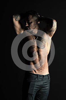 Tattooed man show sexy muscular torso. Sportsman with six pack and ab. Bodybuilder with biceps and triceps. Fashion