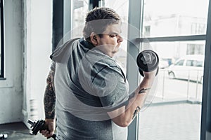 Tattooed man with towel exercising with dumbbells at sports center