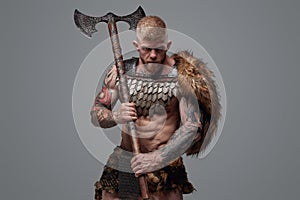 Tattooed muscular viking holding two handed axe on his shoulder