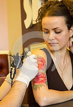 Tattooer showing process of making a tattoo on young beautiful hipster woman with red curly hair arm. Tattoo design in the form of