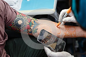 Tattooist with cell phone and pencil making design on the skin