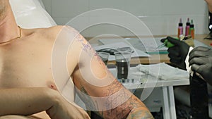 The tattooist makes the tattoo on man`s arm in tattoo salon