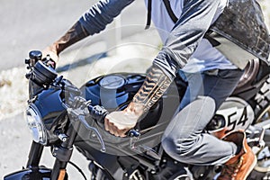 Tattoos on arms of motorcycle rider on custom made scrambler sty