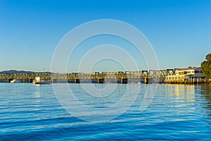 Tauranga Railway bridge catches glow from sunrise in distance across  blue calm water