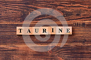 Taurine word lettering made of wooden cubes on dark rustic wooden background. Taurine helps to improve energy metabolism in the