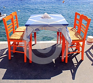 Tavern with orange wooden chairs by the sea coast, Santorini