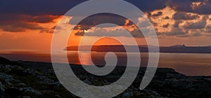 Tawny and cloudy Sunset silhouetting Gozo Island