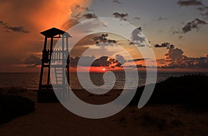 Tawny cloudy sunset silhouetting life guard post watch tower