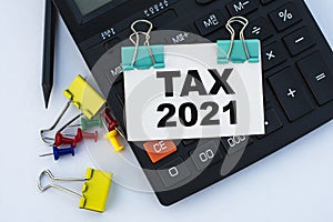 TAX 2021 - words on a white sheet with clips on a white background with a calculator, buttons and yellow stationery clips