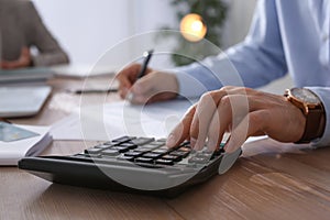 Tax accountant with calculator working at table in office, closeup