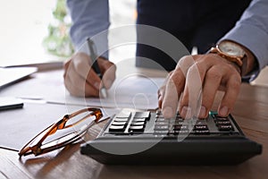 Tax accountant with calculator working at table in office, closeup