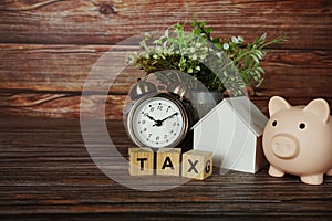 Tax alphabet letter with house model, piggy bank and alarm clock on wooden background