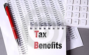 TAX BENEFITS text on notebook with pen, calculator and chart on grey background