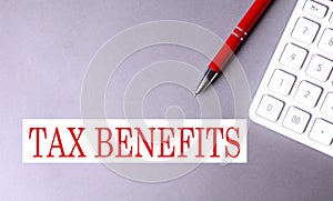 TAX BENEFITS text written on a gray background with pen and calculator