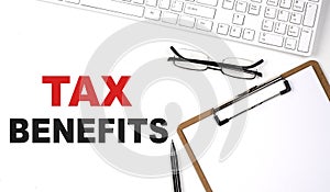 TAX BENEFITS text written on the white background with keyboard, paper sheet and pen