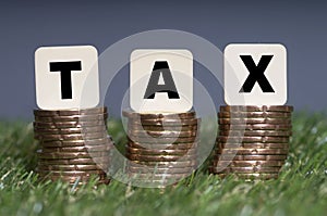 Tax Concept with tax word on stacked gold coins and green grass