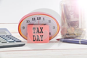 TAX DAY CONCEPT; Clock,red note,calculator and coins in the mason jar over wooden background.