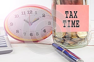TAX DAY CONCEPT; Clock,red note,calculator and coins in the mason jar over wooden background.