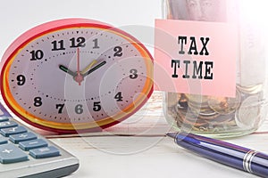 TAX DAY CONCEPT; Clock,red note,calculator and coins in the mason jar over wooden background.