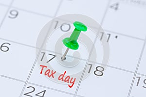 Tax day written on a calendar with a green push pin to remind yo