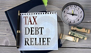 TAX DEBT RELIEF - words in a white notebook on the background of an alarm clock and a banknote
