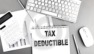 TAX DEDUCTIBLE text written on notebook on grey background with chart and keyboard , business concept