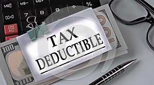 TAX DEDUCTIBLE - words on a white piece of paper fixed on banknotes against the background of a calculator, glasses and pen