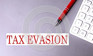 TAX EVASION text written on a gray background with pen and calculator