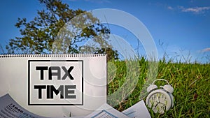 Tax-filling concept - Tax time words on notepad with the U.S IRS 1040 form and clock in nature background