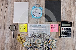 Tax form 1040, dollars, calculator and blue alarm clock on a wooden table.View from above