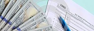 1065 tax form lies near hundred dollar bills and blue pen on a light blue background. US Return for parentship income