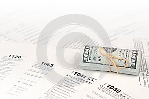Tax forms lies near roll of hundred dollar bills. Income tax return