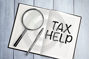 tax help word on notepad with magnifier on wooden background