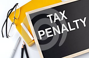 TAX PENALTY text on the blackboard with notepad , pen, pencil
