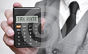 TAX RATE word text inscription on calculator in a male hand of a businessman in white shirt and blue tie, Concept of finance and