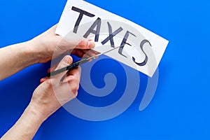 Tax reduce concept. Hands with sciccors cut paper with word Taxes on blue background top view copy space