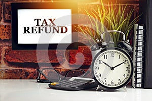 TAX REFUND text with alarm clock, books and vase on brick background