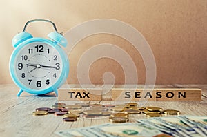 `Tax season` and a blue alarm clock on the table. dark wooden plank background with copy space. The inscription on the wooden bloc