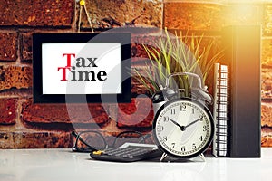 TAX TIME text with alarm clock, books and vase on brick background