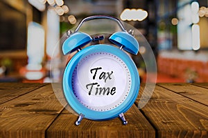 Tax time text on Alarm Clock on wooden table.