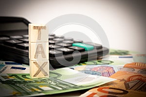 Tax word writen on wooden cubes. Euro banknotes Laid out in a semicicircle and calculator.Copy space for text.