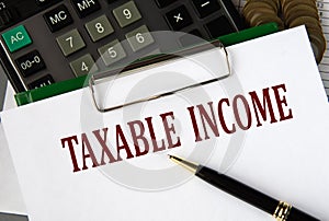 TAXABLE INCOME - words on a white sheet on the background of a calculator and a pen photo