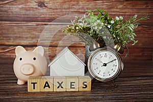 Taxes alphabet letter with house model, piggy bank and alarm clock on wooden background